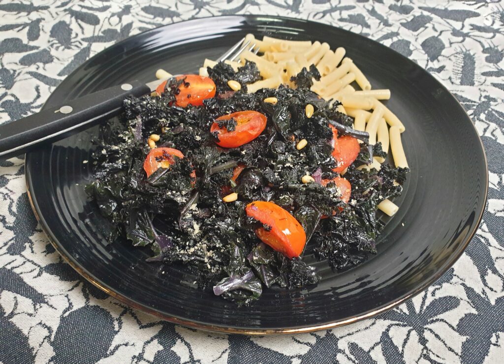 Paarse boerenkool met tomaatjes en pasta op een zwart bord