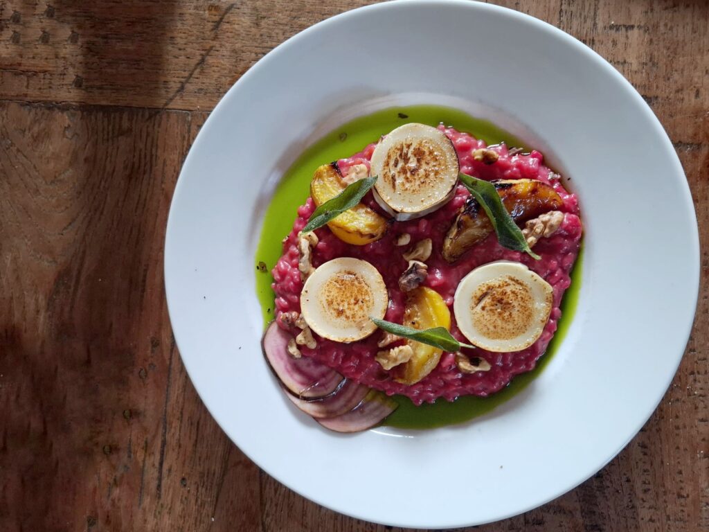 een roze bietenrisotto met gele geroosterde bietjes en gestreepte  gemarineerde chioggabietjes, geitenkaas, salie en walnoten