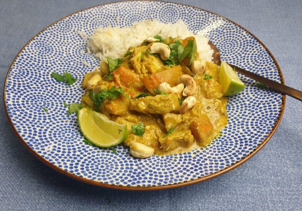 curry van pompoen en jackfruit, geserveerd met rijst, korinader en een partje limoen
