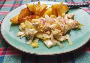 witlofsalade met rode ui, peer , noten en blauwe kaas, daarachter gebakken aardappels
