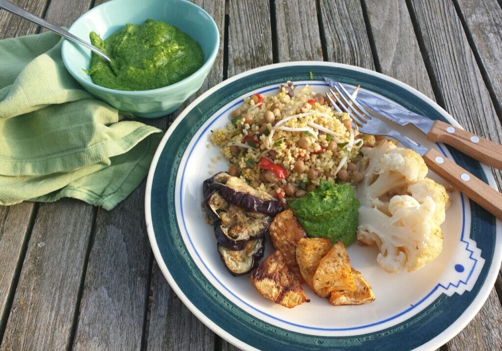 bloemkool, gierstsalade, geroosterde knolselderij en aubergine op een bord, samen met frisgroene peterseliepesto
