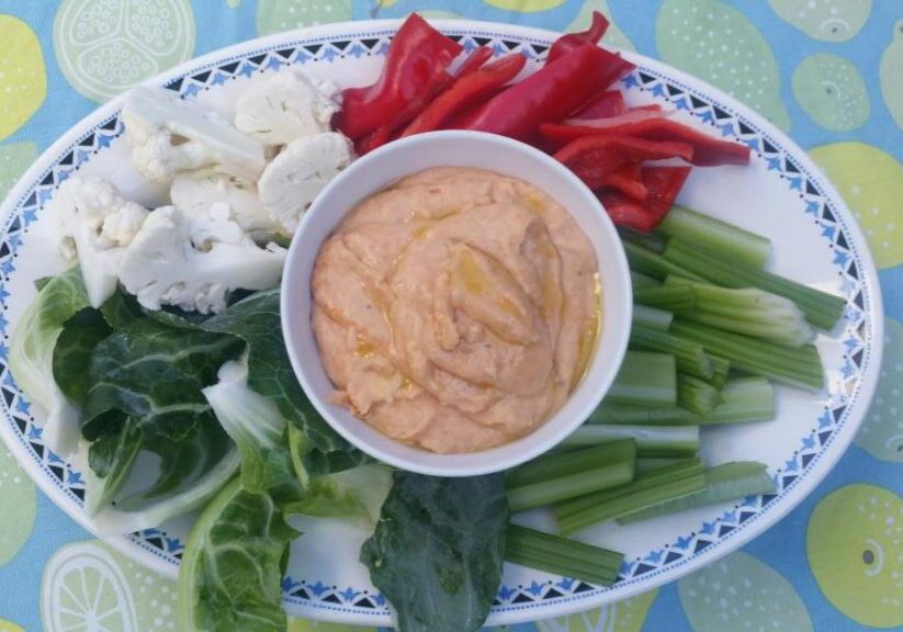 een schaal met stukjes rauwe bleekselderij, paprika, bloemkoolroosjes en bloemkoolbkad en een bonendipsaus in het midden