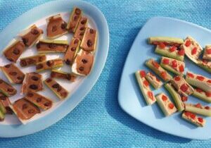 bleekselderijstengels gevuld met pindakaas en rozijnen en met hummus en stukjes rode paprika