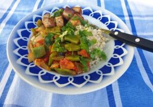 snijbonen in een sausje met tomaat en ui, geserveerd met rijst en gebakken tofu blokjes
