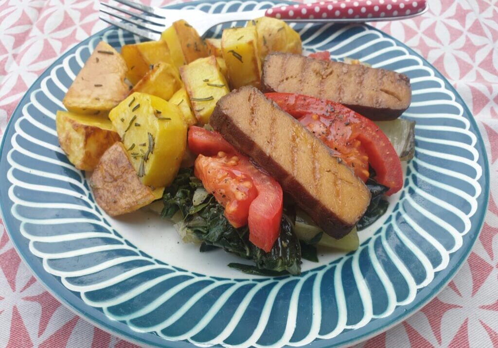 gestoofde snijbiet met tomaat en gegrillde tofu , op een bord met gebakken aardappels erbij 